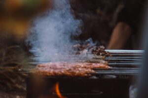 Tasty meat skewers grilling over open flame with smoke rising, showcasing outdoor cooking ambiance.